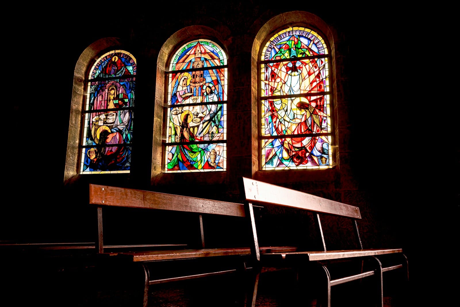 Photo by Philippe BONTEMPS Three stained glass windows above empty church pews